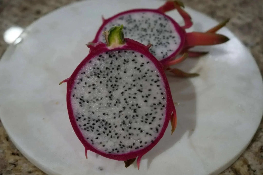 Sliced white-fleshed dragon fruit with pink skin and black seeds on a marble plate