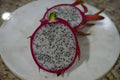Sliced white-fleshed dragon fruit with pink skin and black seeds on a marble plate