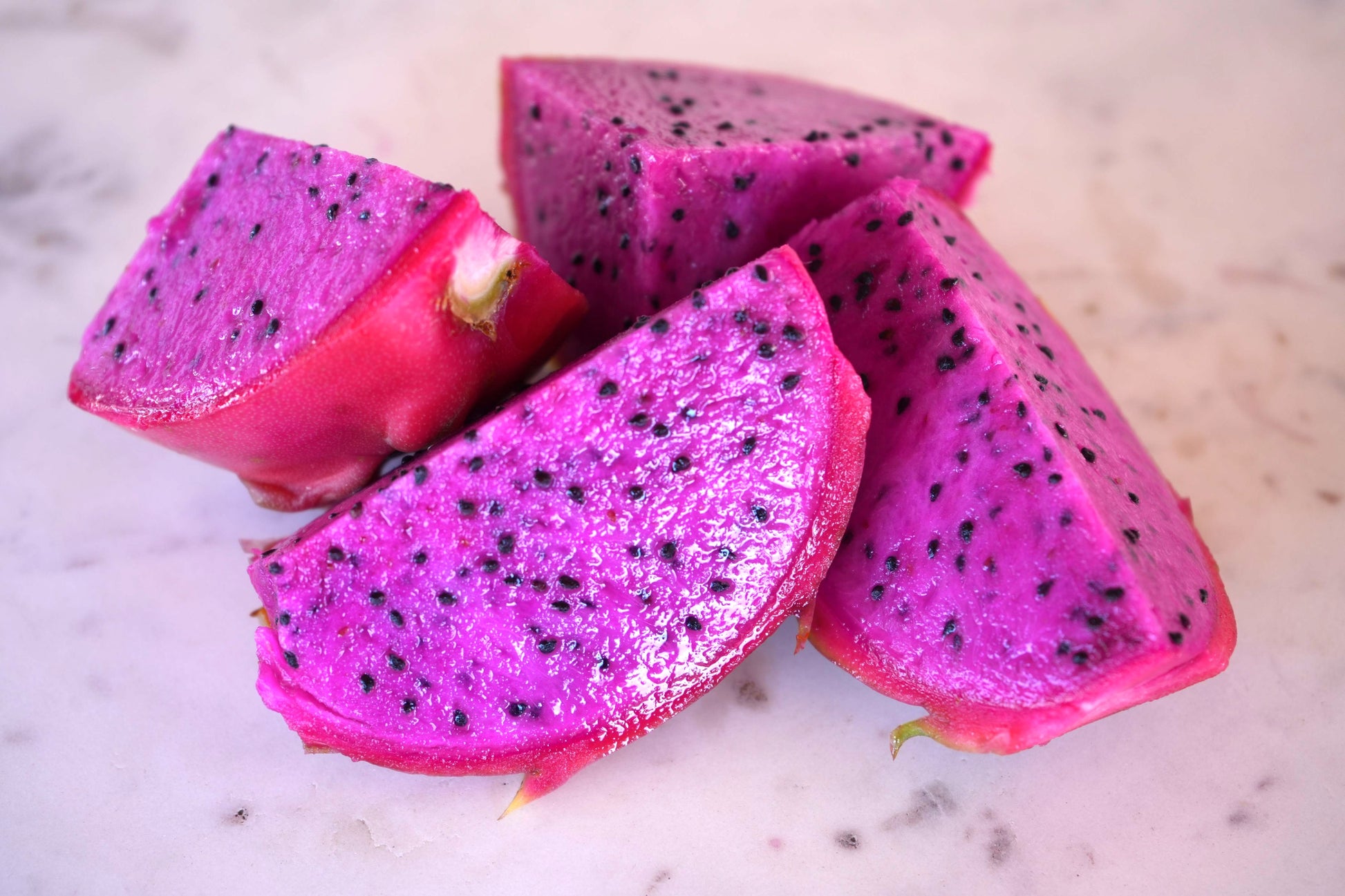 Fresh slices of vibrant purple dragon fruit with black seeds on a marble surface