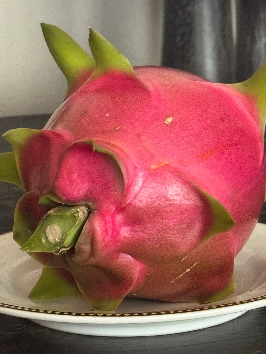 Ripe pink dragon fruit with green scales on a white plate, exotic tropical fruit close-up