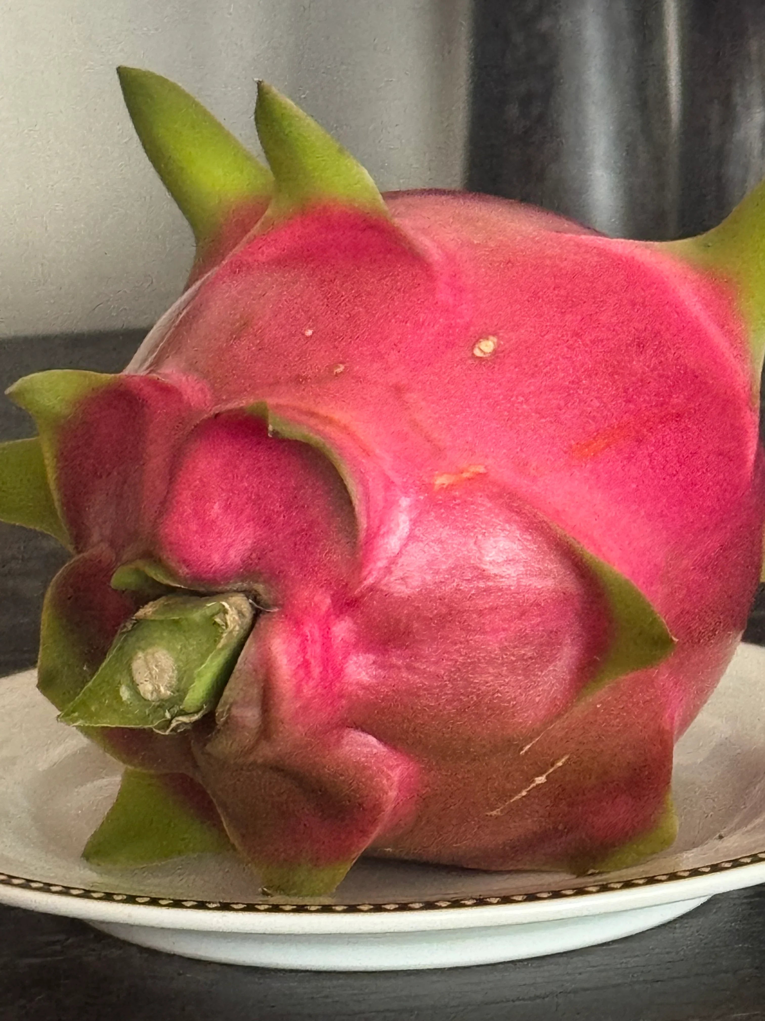 Ripe pink dragon fruit with green scales on a white plate, exotic tropical fruit close-up